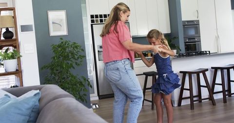 Mother and daughter dancing in sunlit kitchen, playful family moment, cozy home