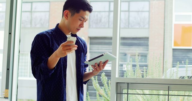 Young Professional Working on Tablet and Smartphone near Window - Download Free Stock Images Pikwizard.com