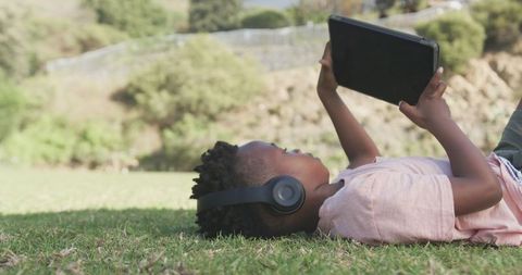Boy Relaxing Outdoors Using Tablet and Headphones in Park