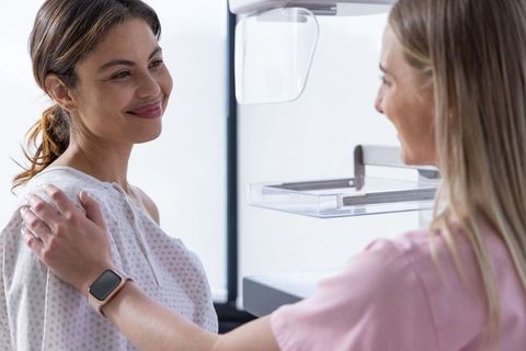 Female patient receiving mammogram care from supportive technologist in bright clinic