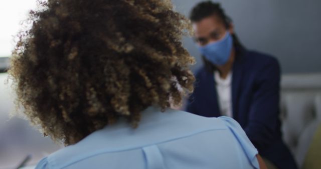 People in a workplace wearing masks and maintaining social distance during a discussion. This can be used in articles, blogs, and websites discussing pandemic protocols in the office, workplace health and safety, or remote working alternatives and logistics.