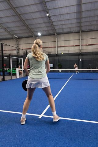 Female paddle tennis players on indoor blue court returning shot under arena lighting
