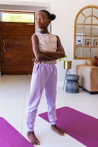 Confident african girl standing arms crossed on purple yoga mat in modern home interior