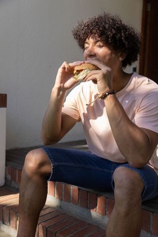 Man enjoying burger outdoors on sunlit front porch steps