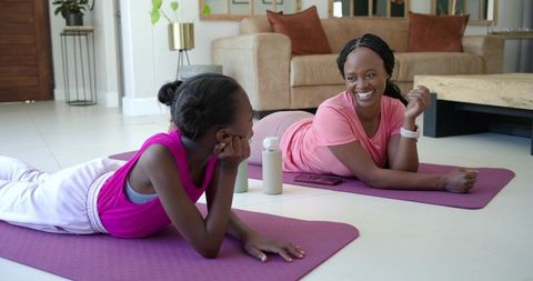 African mother and daughter practicing yoga and chatting on living room mats