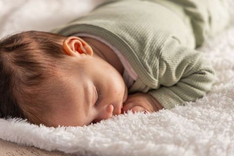 Serene infant sleeping face-down on plush white blanket wearing green ribbed onesie