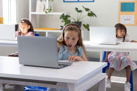 Elementary students working on laptops in bright classroom showing surprise and curiosity