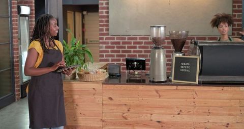 African american baristas serving coffee using tablet at rustic brick and wood counter