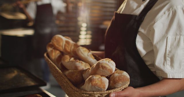 A baker holding a basket of freshly baked bread in a bakery. Ideal for use in food blogs, articles about baking, culinary websites, or advertising for bakery products. Perfect for promoting artisan bread, culinary craftsmanship, and showcasing bakery atmosphere.