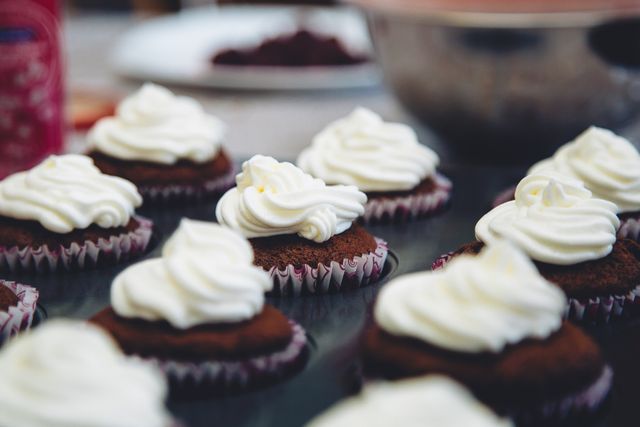 Multiple chocolate cupcakes adorned with cream cheese frosting placed on a kitchen counter. Examples of freshly baked desserts ideal for bakery advertisements, recipe blogs, cooking tutorials, and festive event marketing.