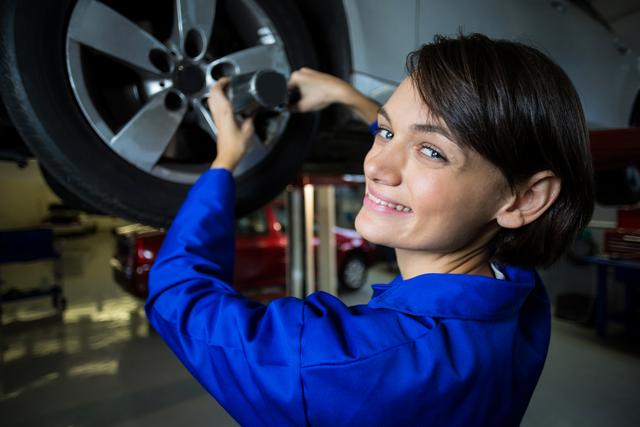 Portrait of female mechanic fixing a car wheel with pneumatic wrench in repair garage