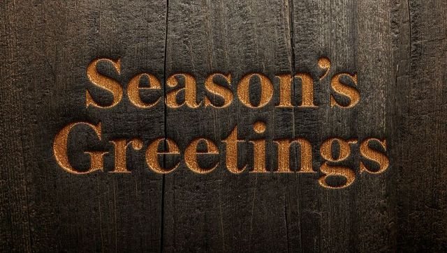 Rustic golden Season's Greetings engraved in dark wood panel with warm glowing relief
