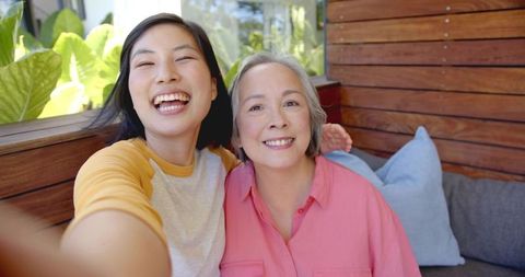 Smiling Daughter Taking Selfie with Mother on Sunny Patio Bench, Family Bonding Moment