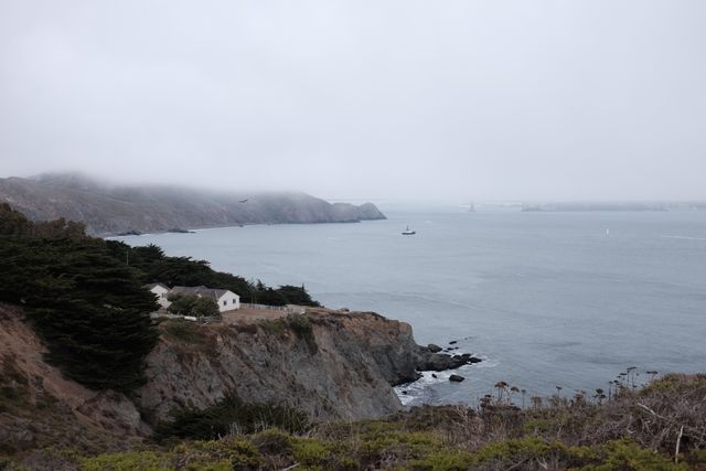 This captures a scenic view of a misty cliff overlooking a calm ocean. The foggy atmosphere and serene ocean create a sense of peace and tranquility, perfect for backgrounds, travel brochures, or promoting nature retreats.