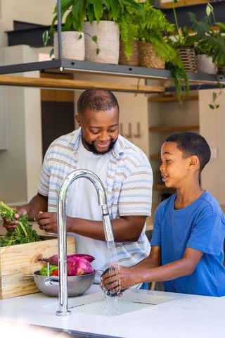 African american father and son washing vegetables at kitchen island with chrome faucet