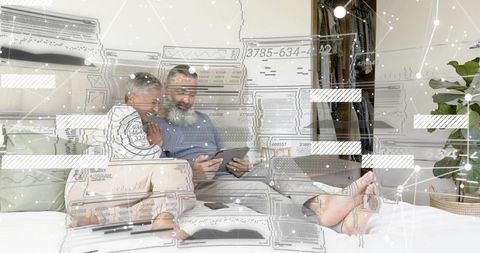 Mature couple relaxing on bed using tablet with holographic data overlay, futuristic tech