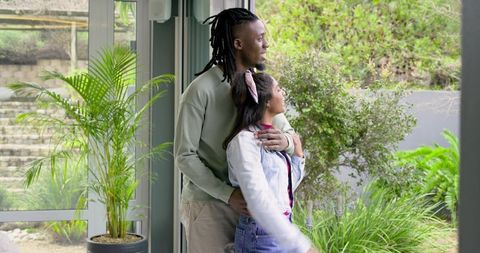 Diverse couple embracing and gazing through sunroom sliding doors into lush garden retreat
