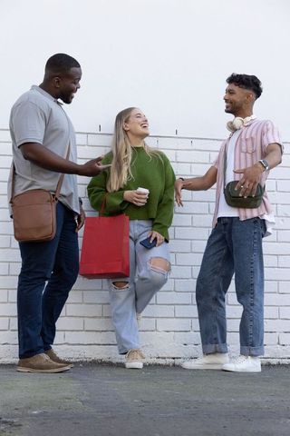 Young friends chatting on urban sidewalk with red shopping bag and coffee