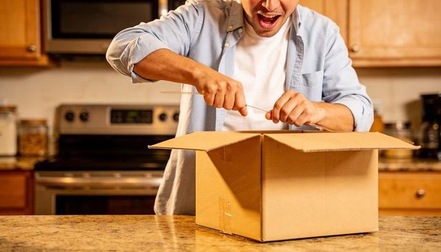 Man Unboxing Cardboard Box on Granite Kitchen Counter Using Tool Excited Home Delivery