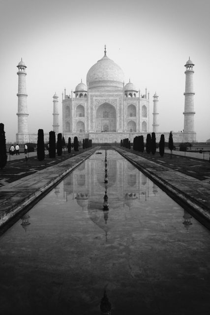 This image captures the majestic Taj Mahal in a stunning black and white composition, emphasizing its architectural beauty with a serene reflection in the foreground water. Perfect for cultural studies, travel articles, historical documentaries, and emphasizing the timeless beauty of UNESCO World Heritage Sites.