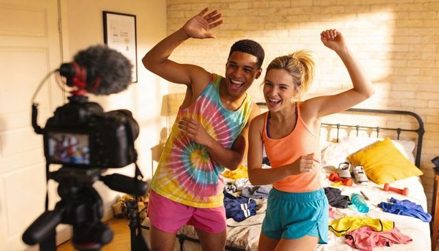 Energetic young couple recording fitness vlog in messy bedroom wearing colorful activewear