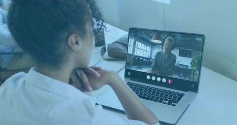 Woman in video call at home workspace with laptop and notes