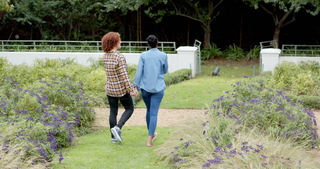 Rear view of happy diverse couple talking, holding hands and walking in garden, copy space. Romance, relationship and healthy lifestyle, unaltered.