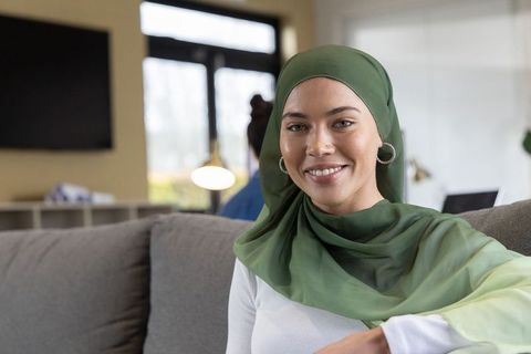 Smiling woman wearing green hijab working on laptop in modern coworking lounge