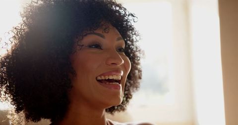 Joyful woman with curly hair laughing in sunlit room