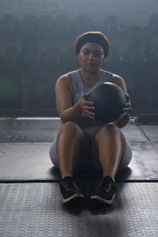African american woman sitting holding medicine ball training core strength gym