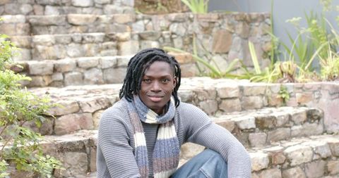 African American man sitting on stone steps in garden wearing sweater and striped scarf