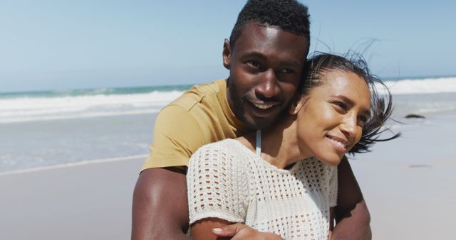 Young African American couple enjoying time together while embracing on a sandy beach. Ideal for advertising romantic vacations, relationship goals, travel brochures, and relaxation themes.