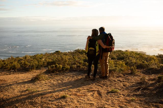 Rear view of a senior Caucasian couple enjoying time in nature together, hiking, taking a break, standing, embracing admiring the sea view