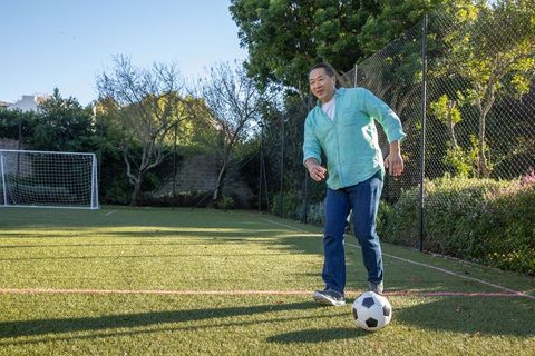 Mature Asian Man Engaged in Leisurely Soccer Practice on Sunny Turf