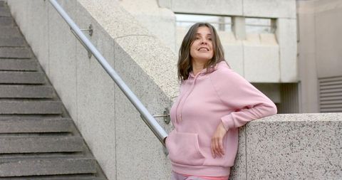 Young woman leaning on concrete balustrade wearing pink hoodie urban minimalist lifestyle