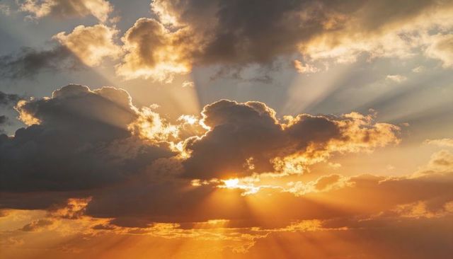 Vibrant golden crepuscular rays breaking through cumulus clouds at sunset over horizon