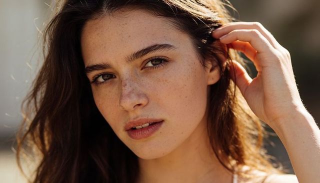 Sunlit freckled woman tucking long hair with hand closeup natural beauty portrait outdoors