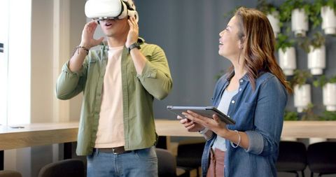 Diverse coworkers testing VR headset while colleague using tablet in modern office