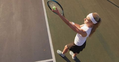 Overhead view of female tennis player serving on hard court, athletic action