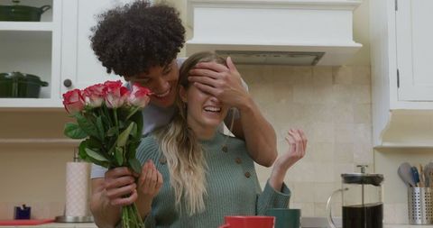 Happy couple sharing romantic surprise with flowers in cozy kitchen