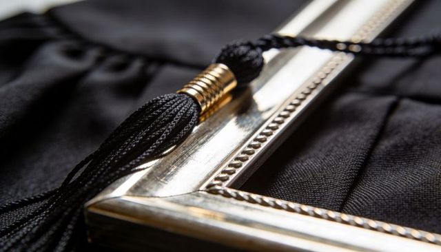 Silver diploma frame corner reflecting warm light with black graduation tassel close-up