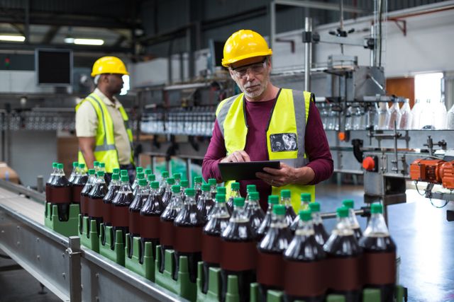 Factory worker with digital tablet monitoring drinks production line at factory