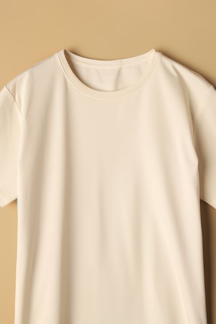 Cream color blank t-shirt isolated against beige background is suitable for clothing store displays, fashion websites, apparel catalogs, or textile design references. Ideal for use in design projects aimed at presenting simple and minimalist styles. Can be used to illustrate topics related to casual wear, dressing, and fashion industry topics.