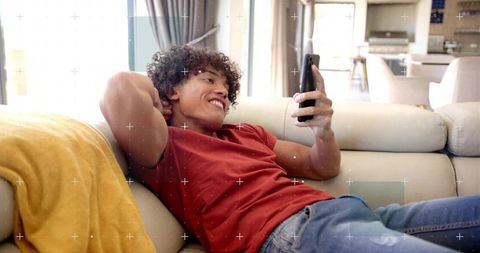 Young man relaxing on sofa scrolling smartphone in modern cozy living room