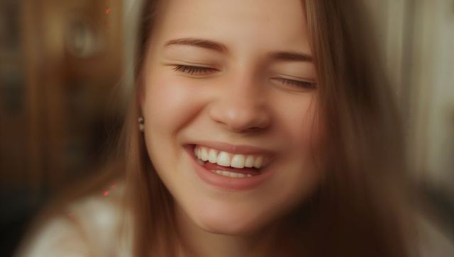Laughing young woman with closed eyes, warm natural smile, intimate closeup