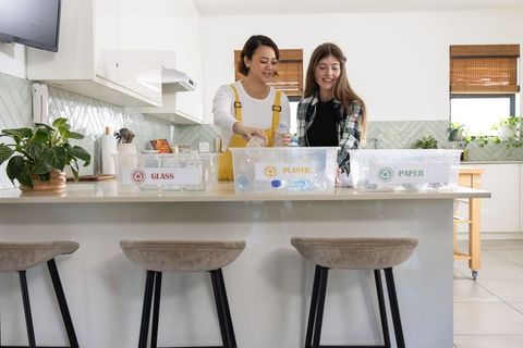 Young women smiling sorting recycling at kitchen island with plastic glass paper bins