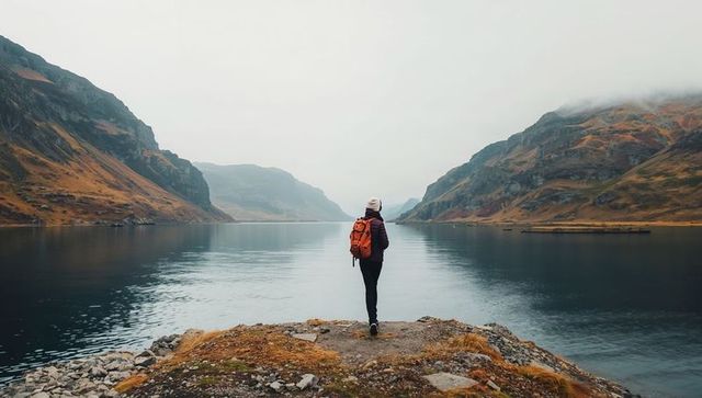 Solitary hiker overlooking misty mountain lake with orange backpack and beanie