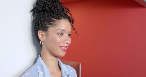 African american woman leaning against wall, poised studio portrait with red background