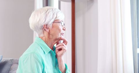 Thoughtful Senior Woman Gazing Through Window Indoors