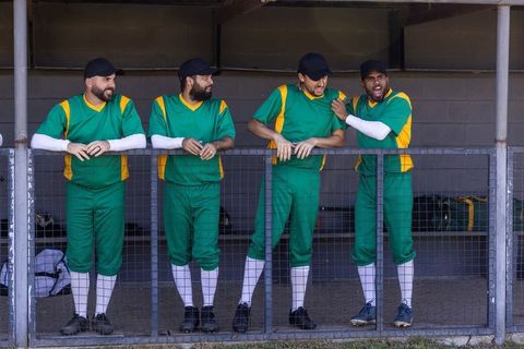 Baseball teammates laughing in dugout wearing green and yellow uniforms — team camaraderie